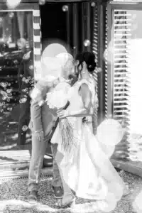 Jeunes mariés chauve et brune s'embrassant tendrement sous une pluie de bulles, bouquet de mariée rustique.