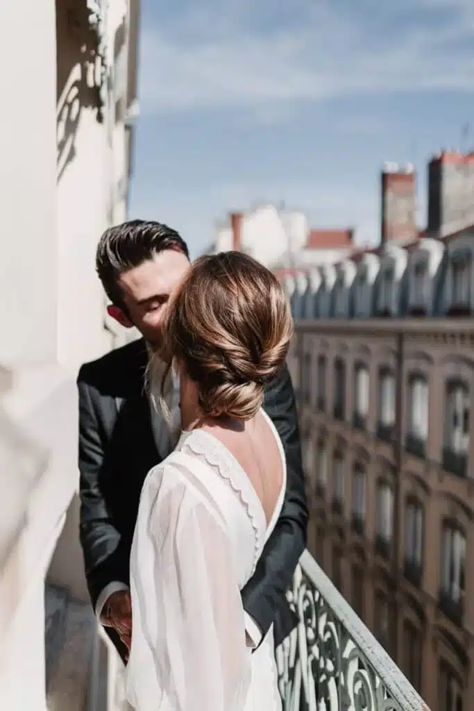 Couple de mariés s’embrassant sur un balcon parisien baigné de soleil