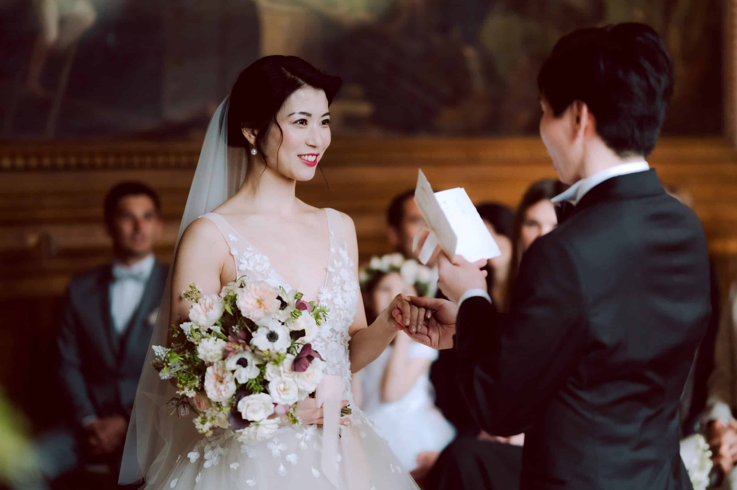 Mariée souriante écoutant les vœux du marié lors d'une cérémonie de mariage avec bouquet floral.